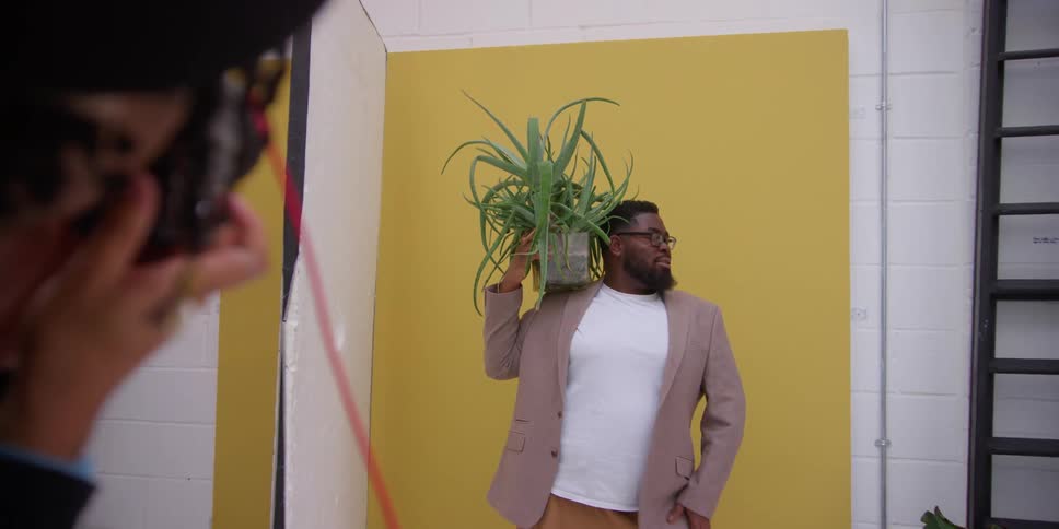 A man photographs another man holding a plant