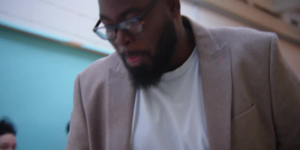 Two black men discuss something while three people stand in the background