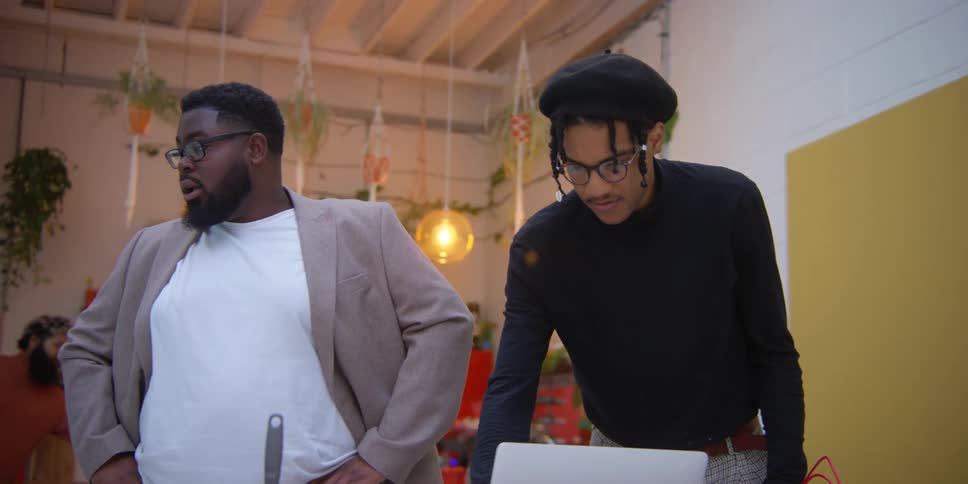 Two men talk while looking at a laptop
