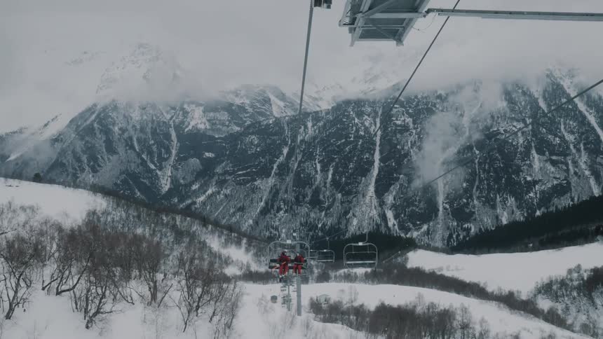 Two skiers take a lift up a mountain