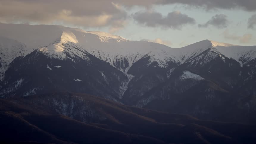A large mountain range towers over forests below