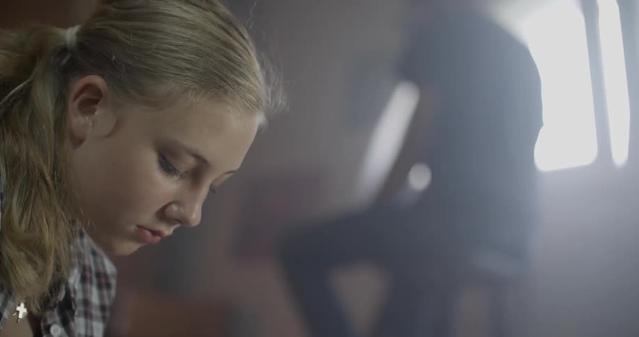 A girl sits with her head down and someone in the background is sitting on a stool