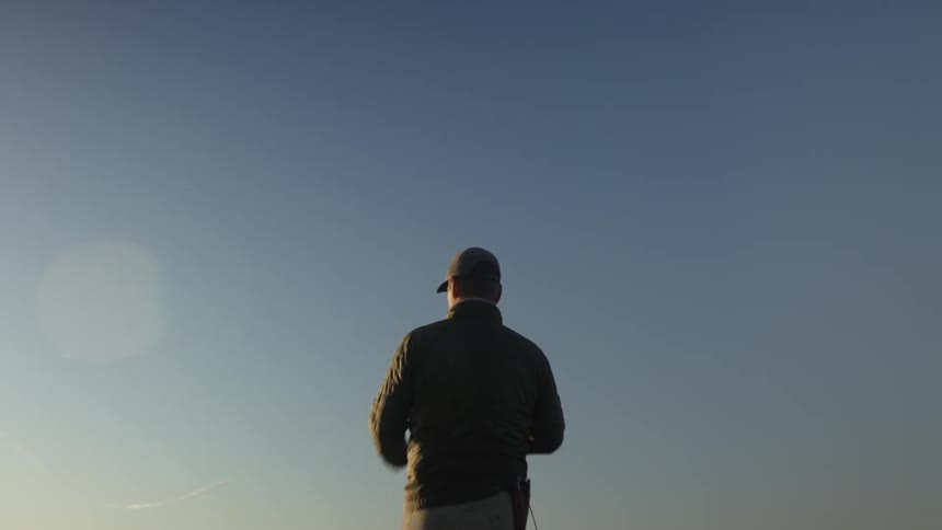 Man with his back casting his fishing rod into the cloudless morning sky