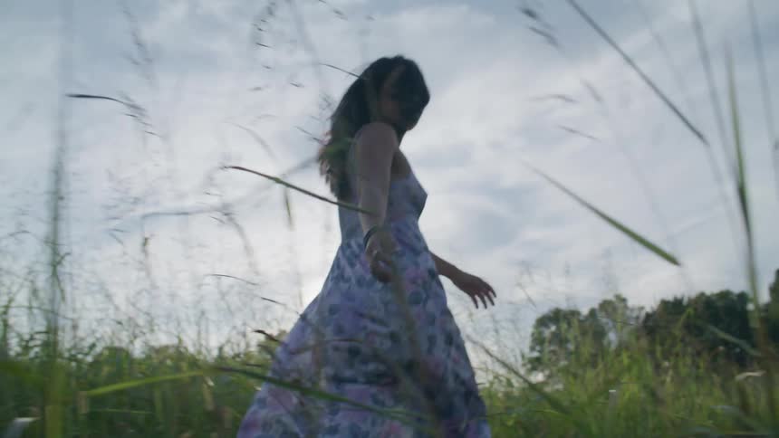 A woman in a dress is walking and jumping over a field with tall vegetation