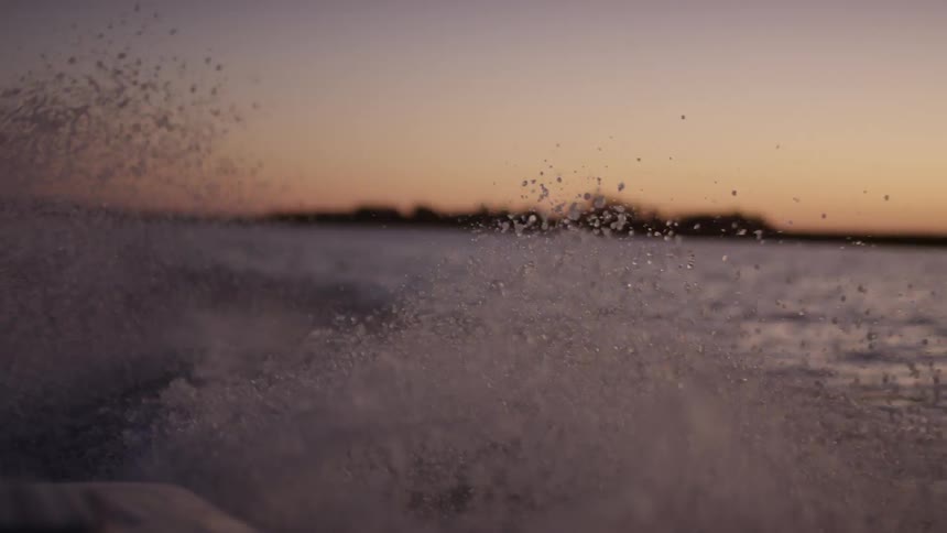Rear view of a small boat in motion repelling water in a purple dawn sky