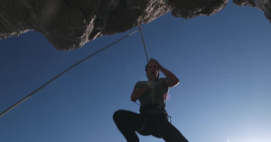 A man is descending from a rock hanging from a rope and behind him to a large ocean