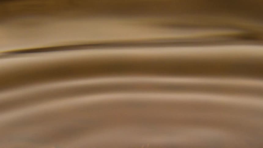 A golden liquid surface is disturbed by a drop in a closeup shot