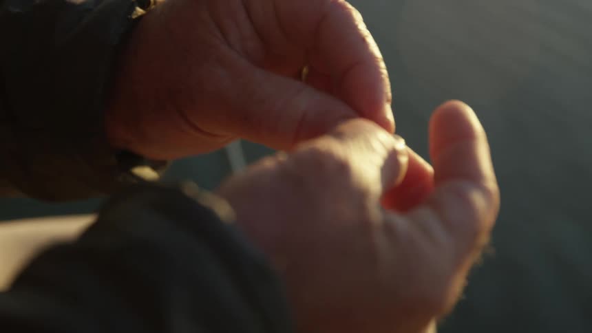 Closeup of a mans hands tying a fishing line in the middle of a river