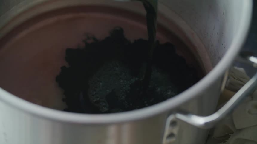 Black liquid being poured into a pan with another liquid