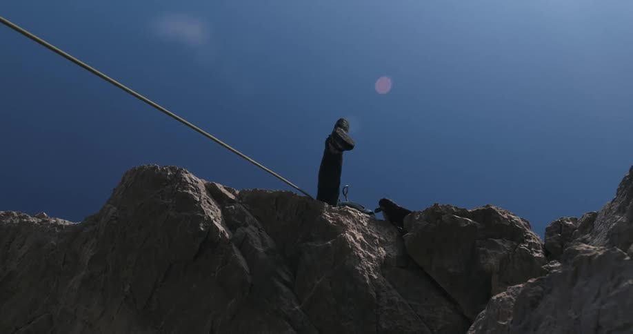 Rock climber moves up cliff using rope on a sunny day