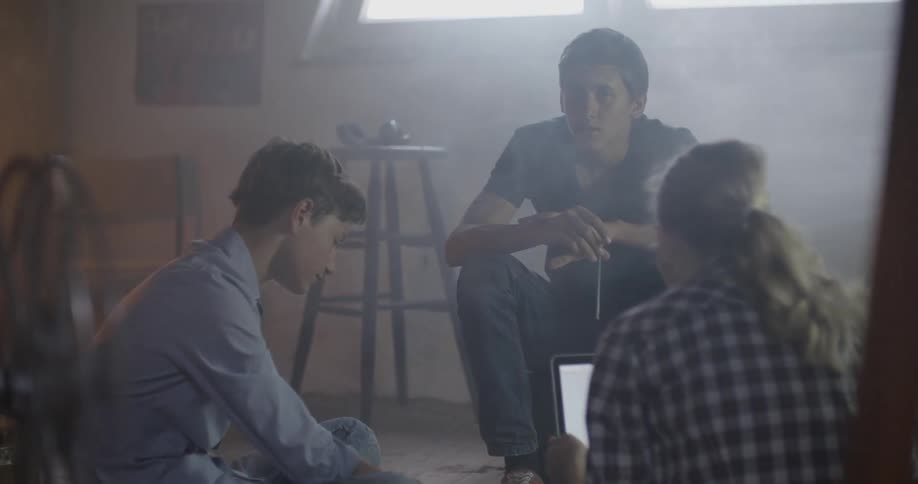 Young people sit in a dim room as a young woman uses a laptop