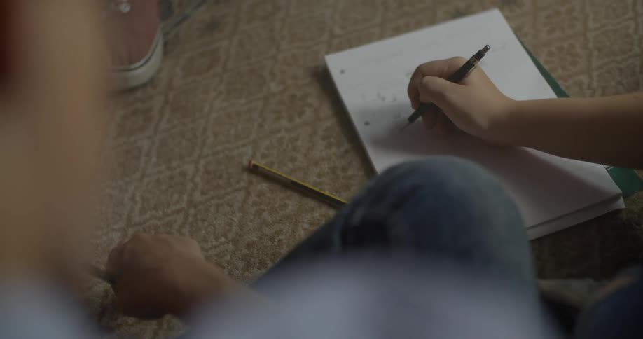 A person is writing in a notebook on the ground