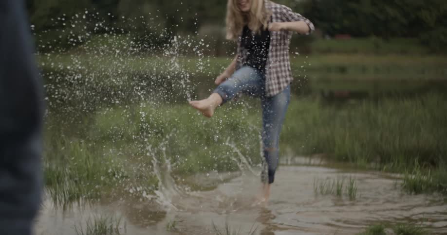 A woman kicks up water at a person standing on the shore as she wades in a pond