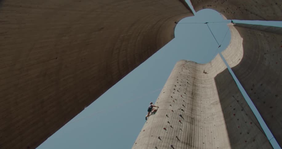 A man climbs a large concrete wall during the day