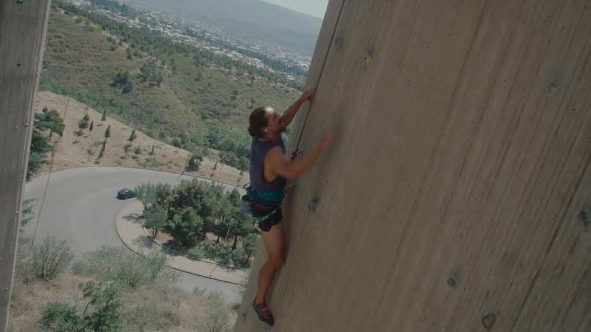 A man climbs a large wall during a hot day