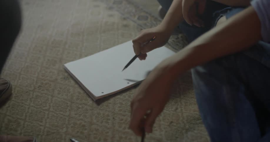 A person crouched down draws a line across a notepad