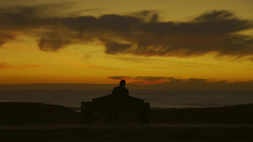 A silhouette of a person sitting and looking at the sea on the horizon on an orange morning