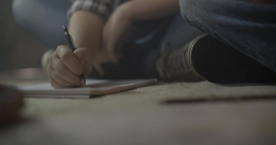 A person sitting on the floor is noting something on a pad of paper
