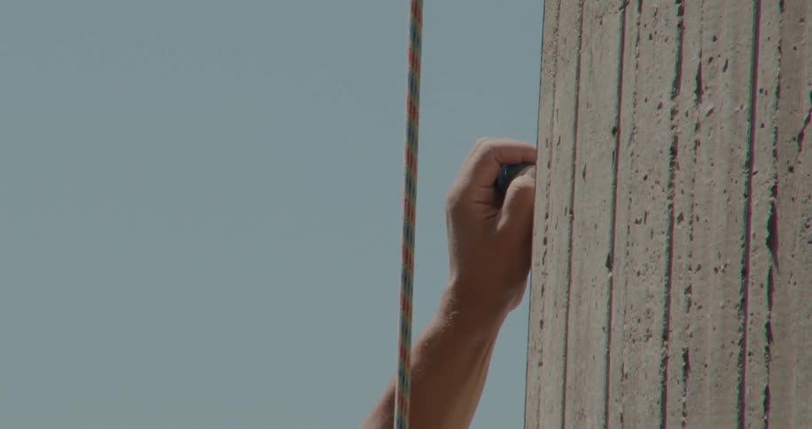 A hand of a person who is climbing holds onto a handhold and there is a rope next to it