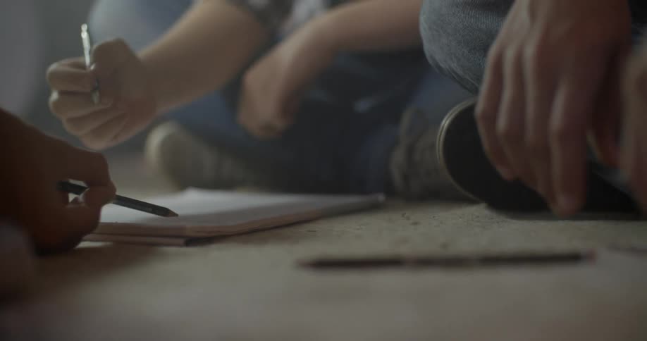 Three people sit on the floor writing in a notebook