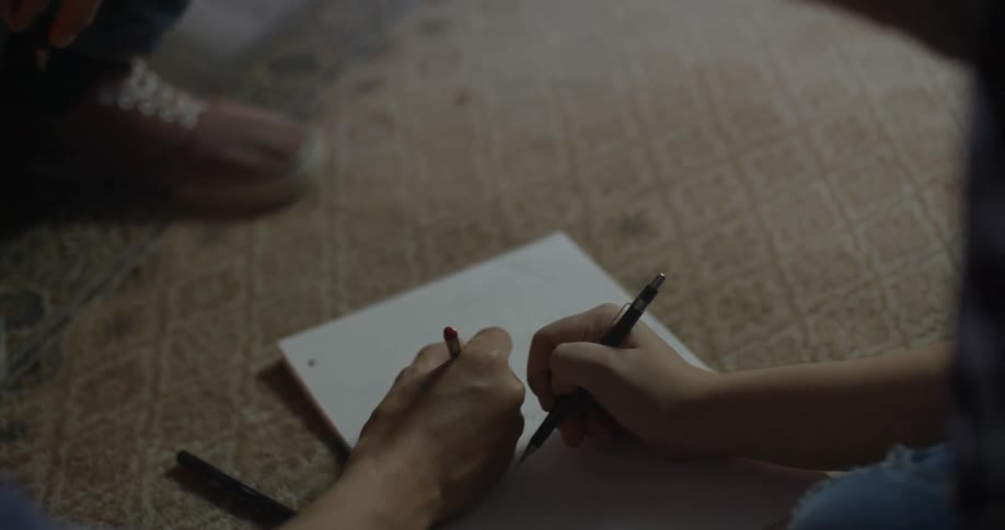 Two people write on a notepad on the floor