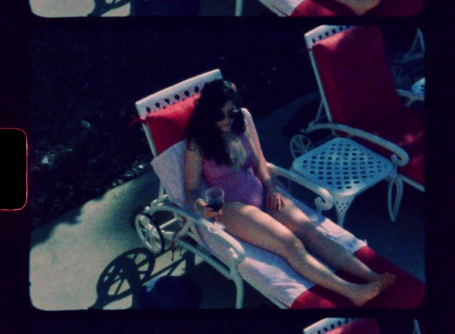 A woman drinking a glass of wine while lying on a beach chair by the pool side