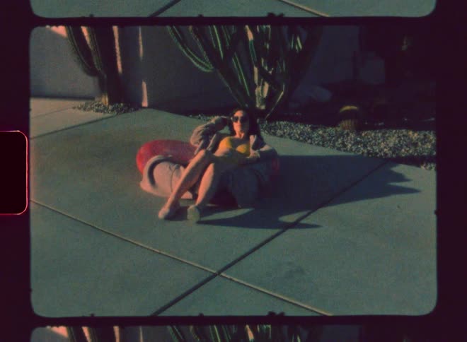 A woman wearing swimsuit on a sunny day lays on a pool ball on the floor while wearing glasses