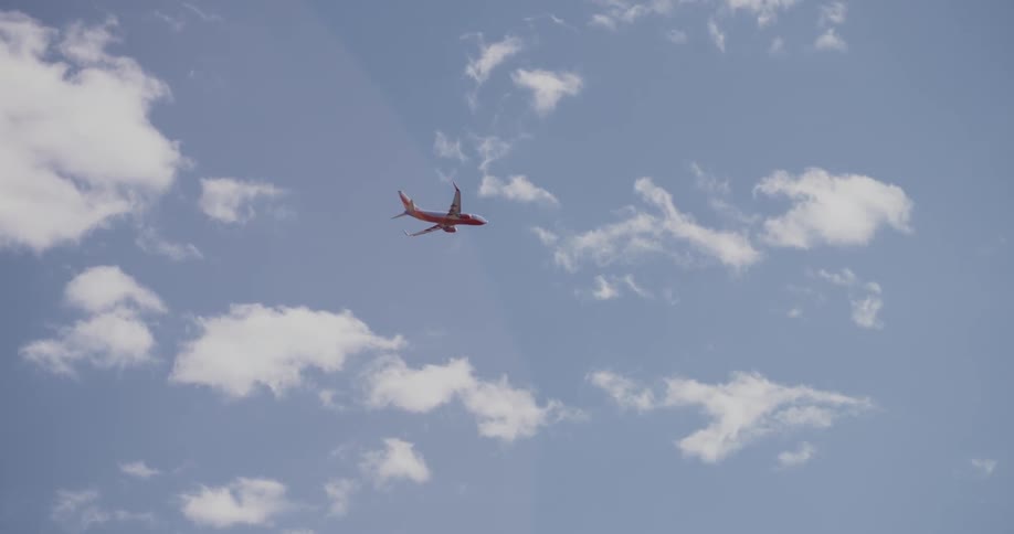 An airplane flies across a blue sky with clouds
