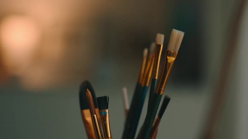 A jar filled with paint brushes sits on a table