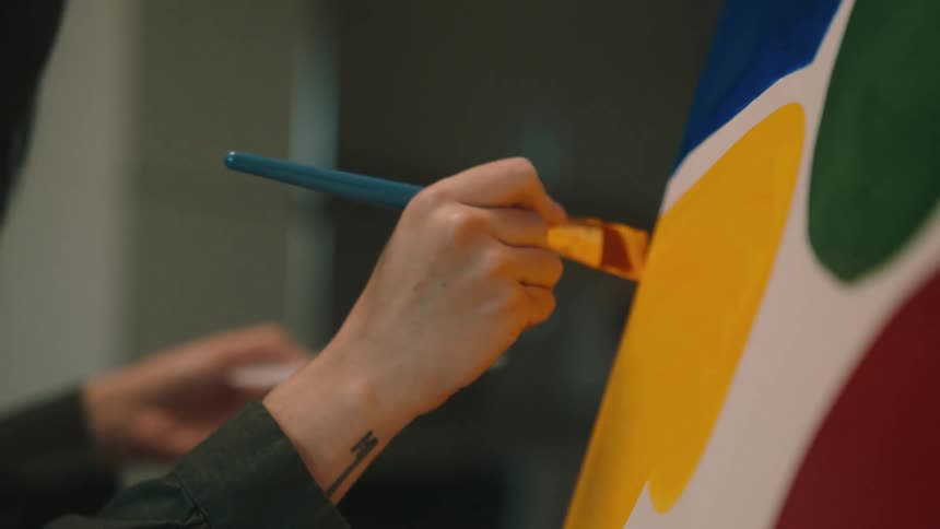 A womans hand holding a paint palette and painting a canvas with a brush