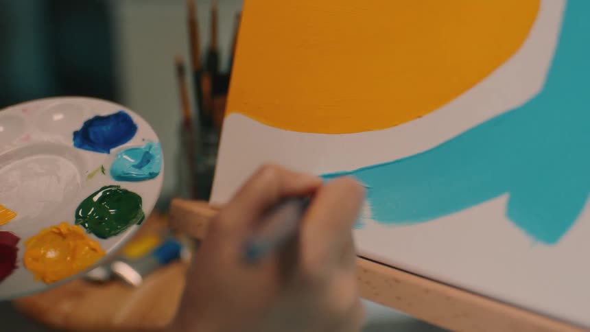 Female artist applies paint to abstract painting on wooden easel