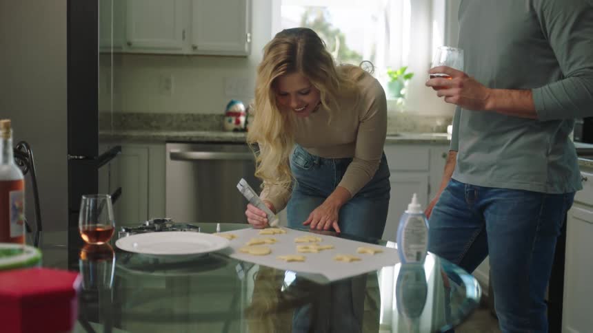 Couple together in the kitchen putting cream on top of smiling and happy shaped cookies