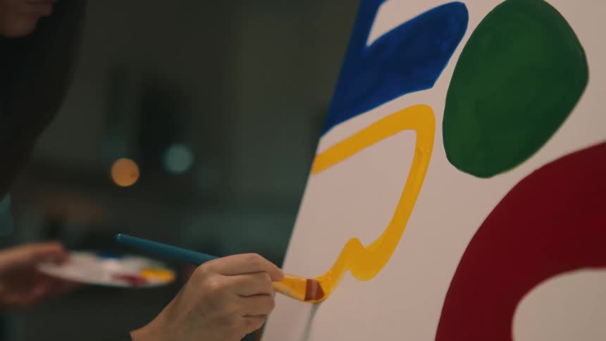 A womans hand holding a paintbrush and painting a canvas