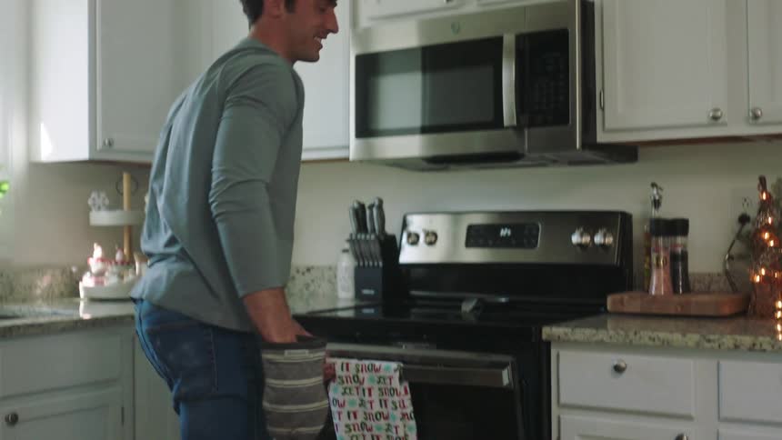 Man putting cookies in the oven and clapping hands joyfully with his wife