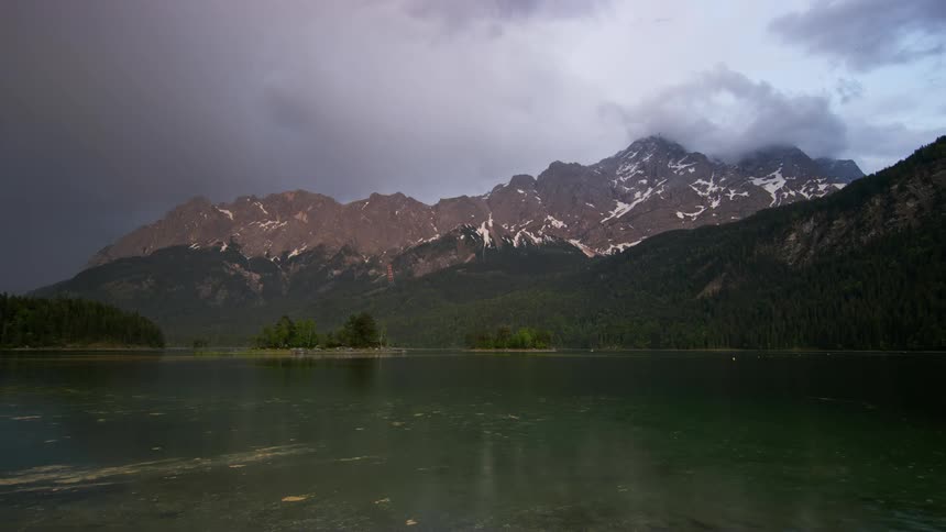 Mountain range covered in clouds next to a lake during day time