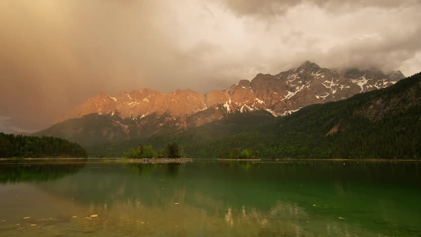 Natural landscape with a wide lake that a forest to one side and a mountain range to the other during day time on a cloudy day