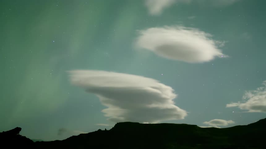 Silhouette of mountains and the sky with darkening clouds with a timelapse of the northern lights