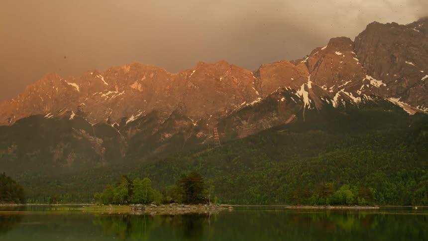 Natural landscape of lake surrounded by a mountain range with forests and trees during day time on a cloudy day