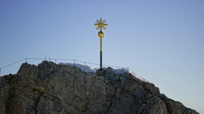 A golden cross stuck on top of a rocky mountain