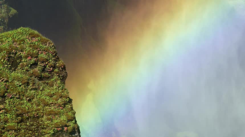 Rainbow colored clouds flow past cliff