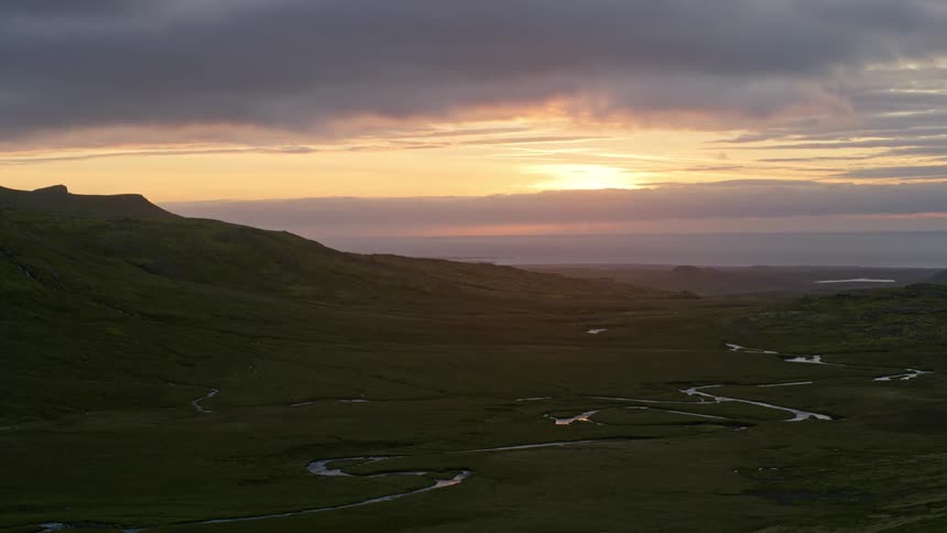 Panorama of a grassland with a river and the sun setting on the horizon