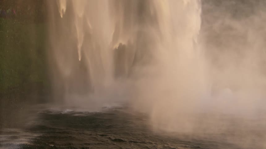 Water flowing into river at base of waterfall creates thick mist
