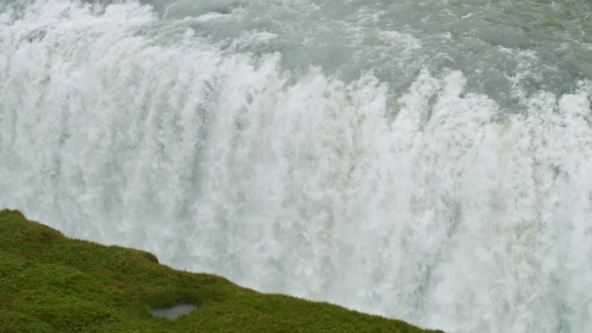 Waterfall outdoors next to a cliff covered in grass during day time