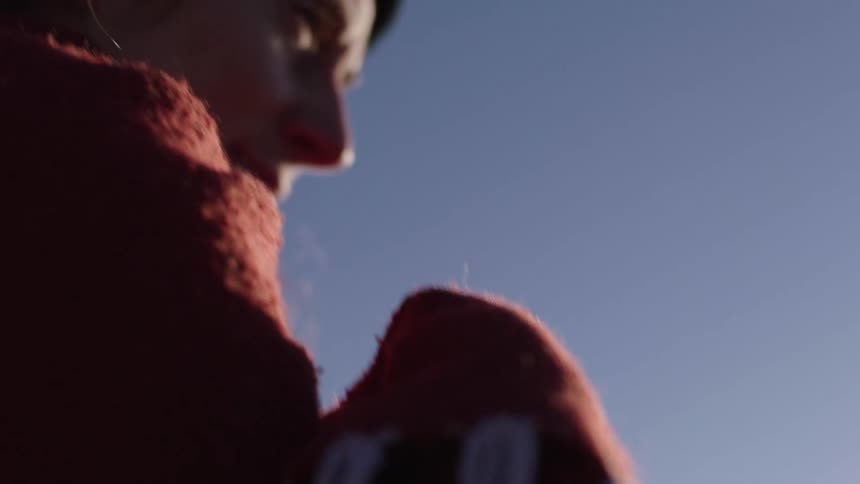 Woman wearing beanie wrapped in shawl stands outdoors under blue sky