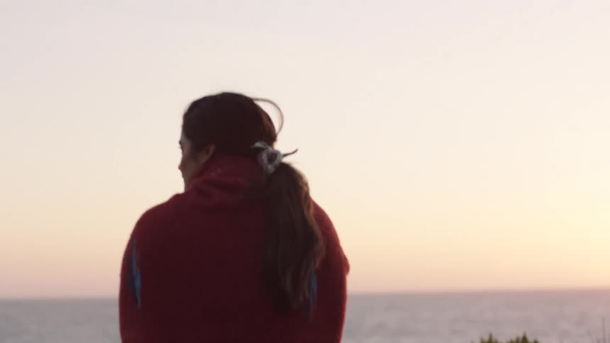 A woman walks along a beachfront trail at sunset