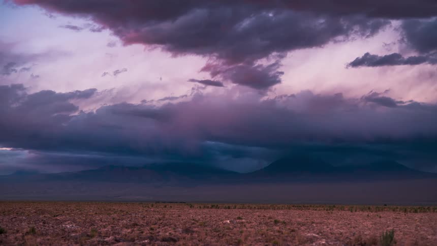 A desert region with some mountains on the horizon and a huge cloud in the sky that is dark