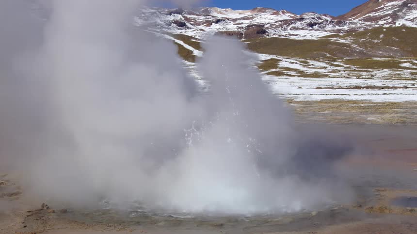 An eruption of water in a thermal lake in the mountainous landscape