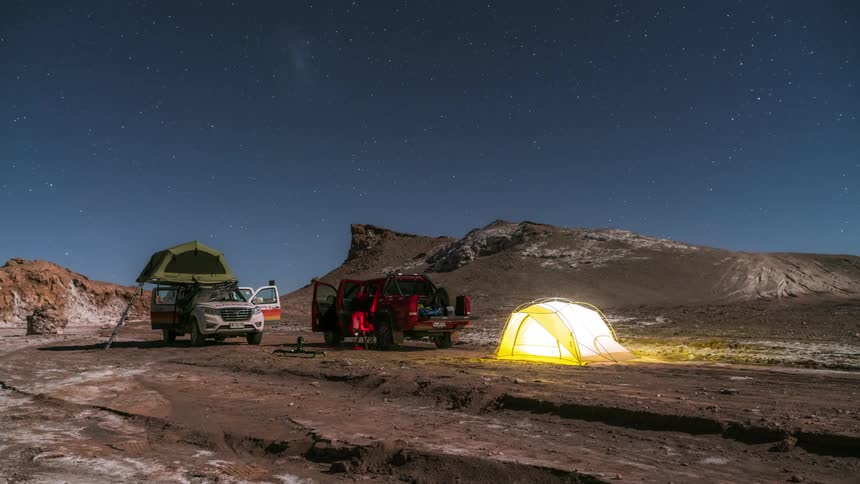 Group of people setting up equipment and tents in the open sky on a timelapse as the day transitions into night
