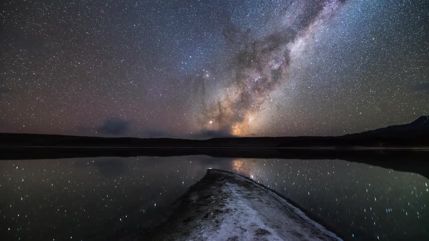Landscape of a sky with nebula and stars reflecting over a lake at night in timelapse