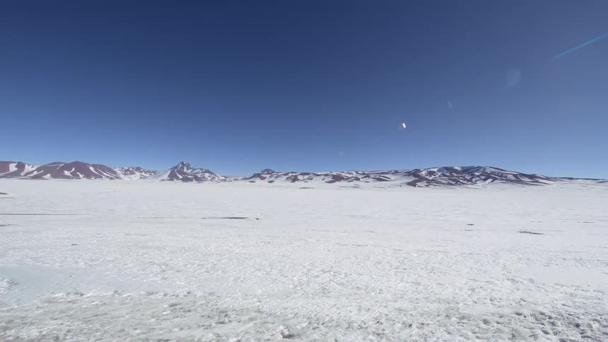 Panorama of snowcovered ground with mountains around and the sun
